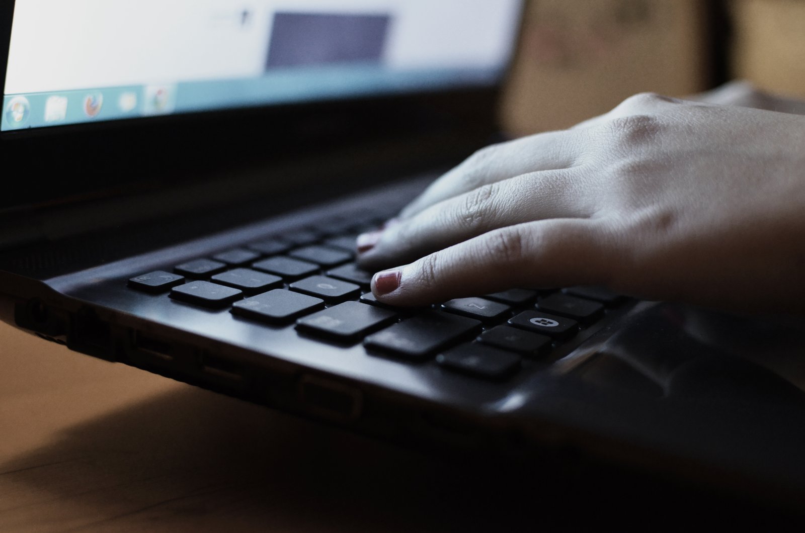 A pair of hands typing on a laptop next to an open paper notebook on a wooden desk, capturing the moment a person decides whether to follow a checklist or hand the task to a tool.