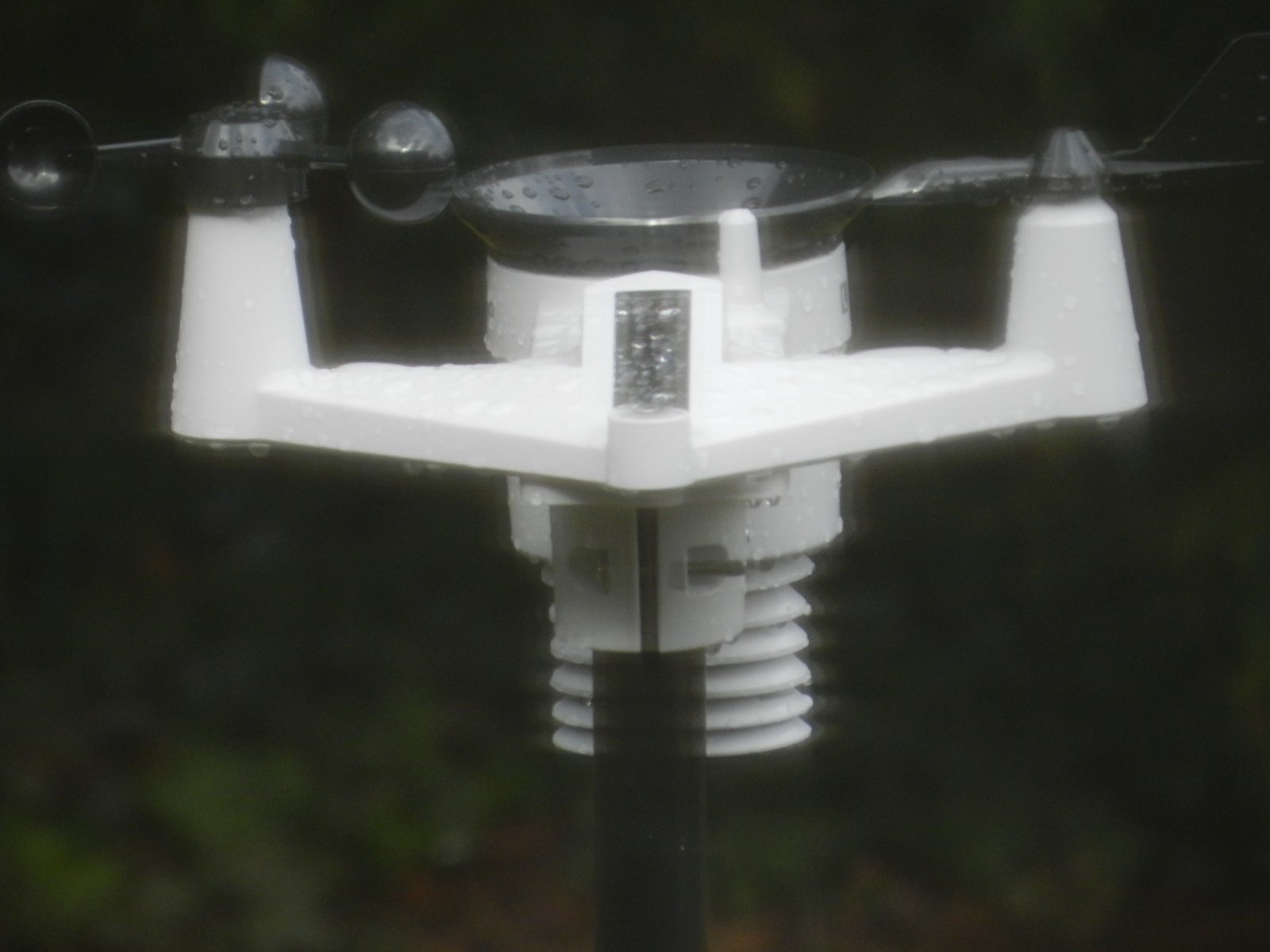 A personal weather station with rain drops on the cups, sensor, and rain funnel, photographed under rain.