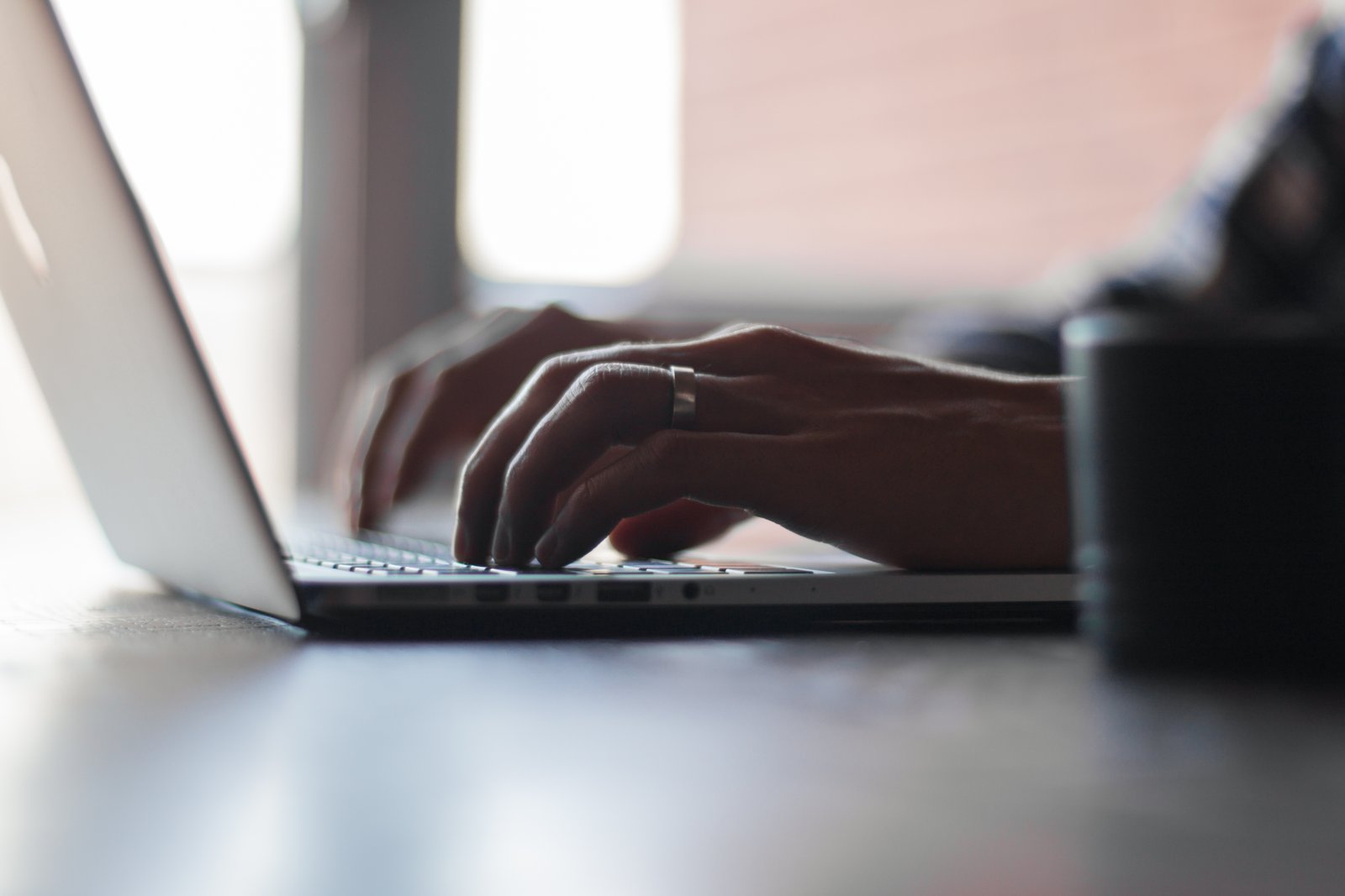 Close-up of hands typing on a laptop keyboard at a desk, shot with shallow depth of field