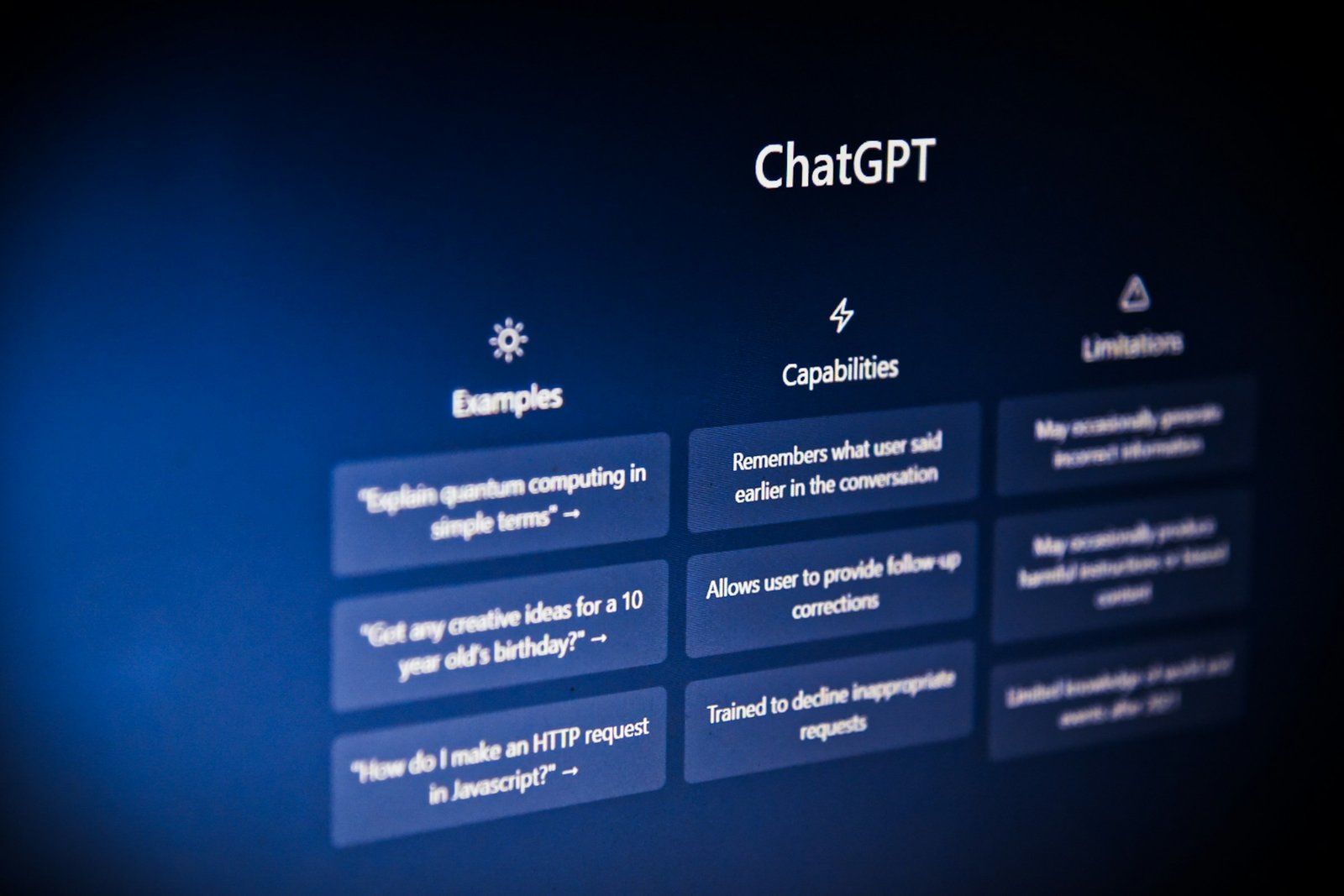 Close-up of the ChatGPT empty-prompt screen, lit deep blue against black, showing the Examples, Capabilities, and Limitations columns - the screen everyone sees the first time they sit down to type a prompt.