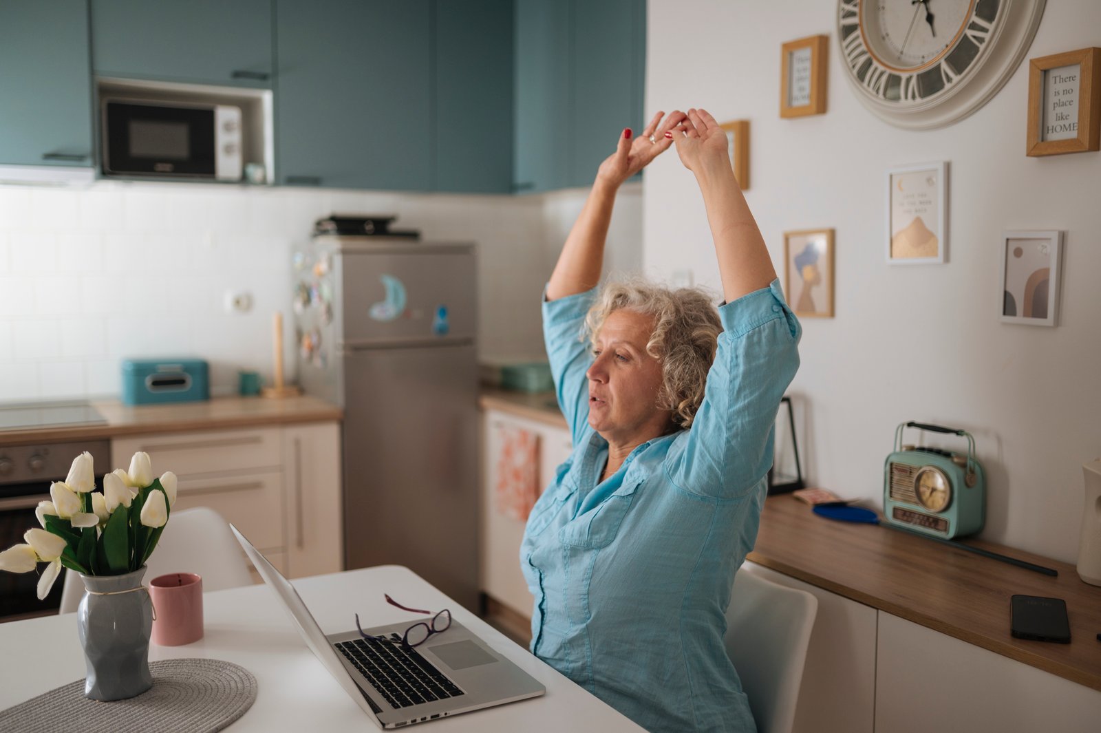 Woman stretches at home office desk while working on laptop