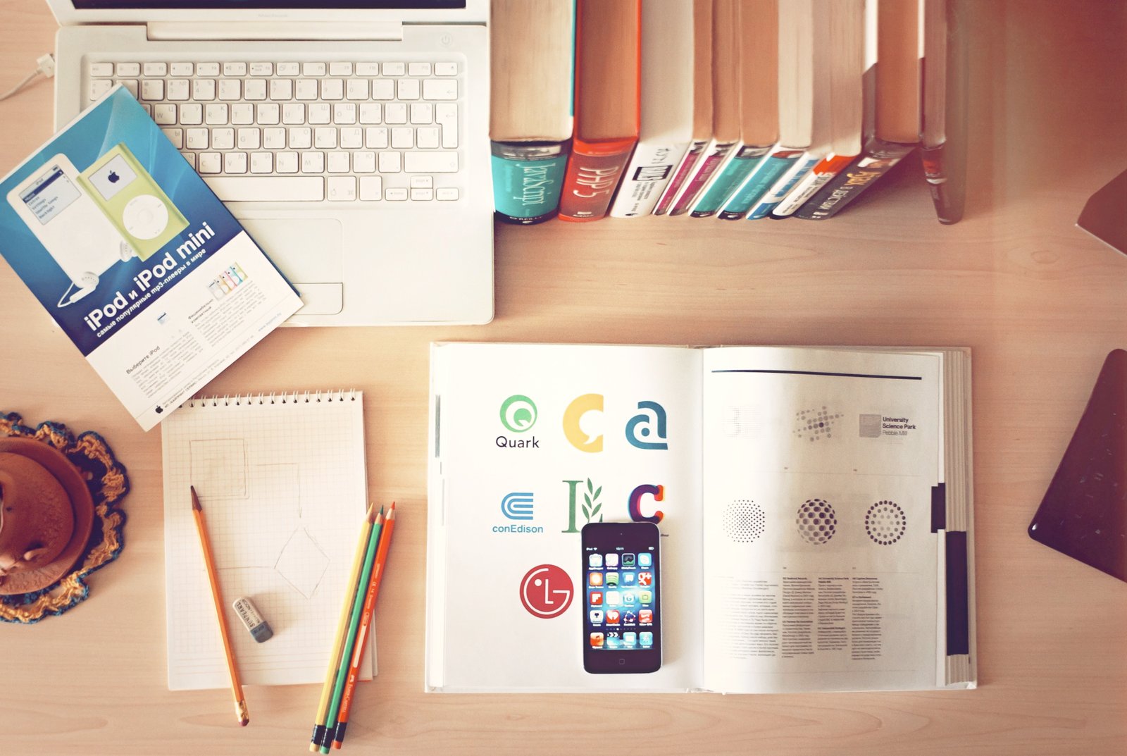 A desk workspace with books, pencils, a laptop, and a smartphone arranged together - multiple information sources at once