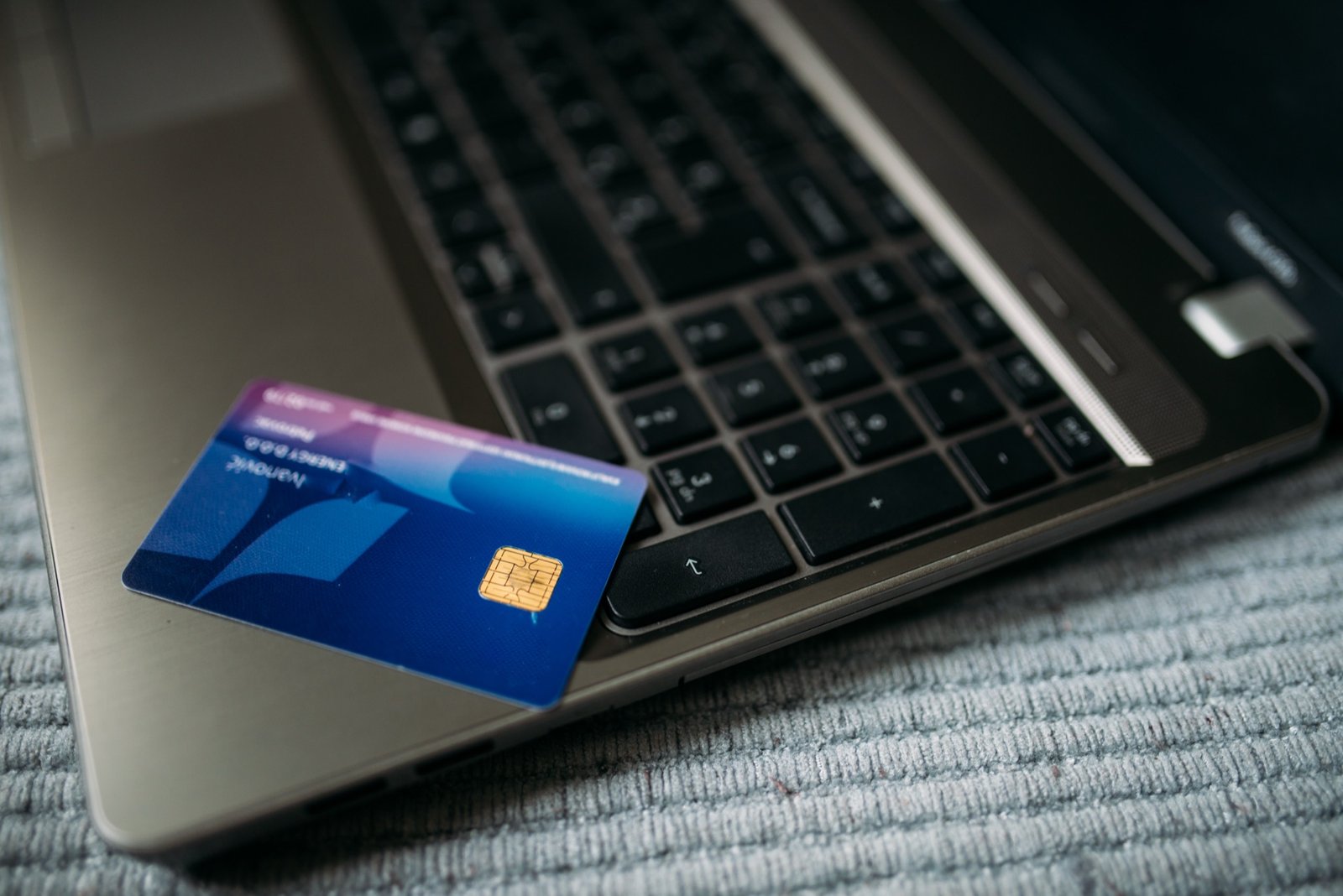 A bank card resting on the keyboard of an open laptop, lit from above.